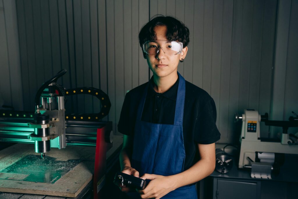 Portrait of a worker in a workshop with CNC machine, wearing safety glasses and apron.